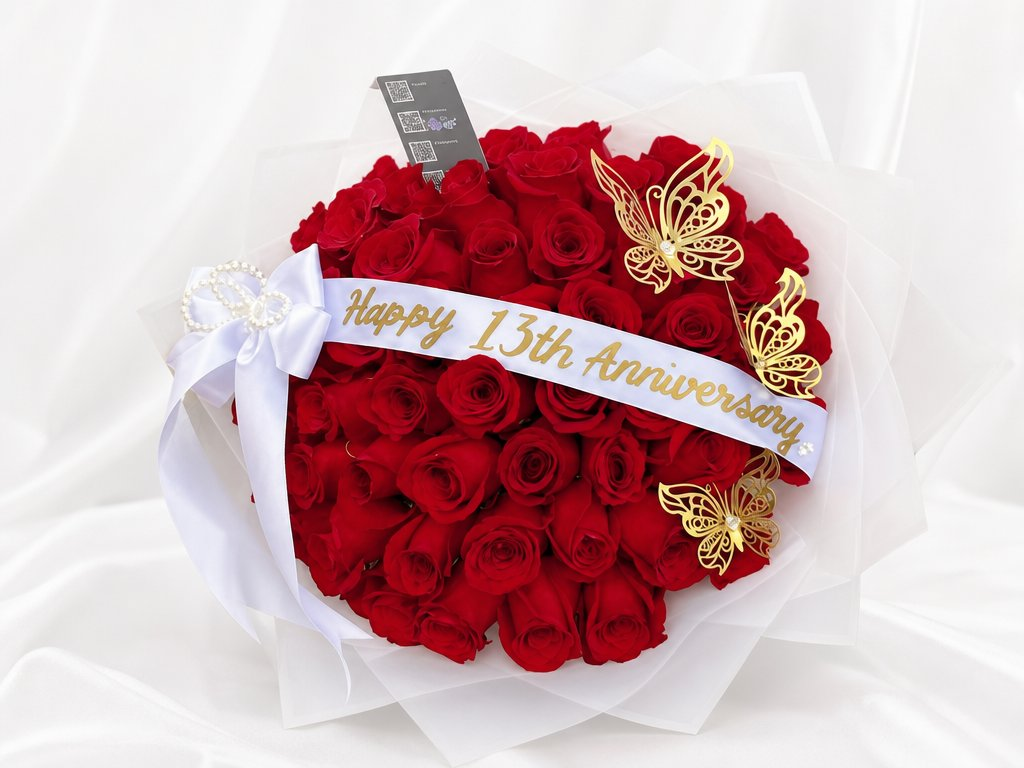 Red roses in white organza wrap with gold butterfly accents, pearl bow, and an anniversary sash