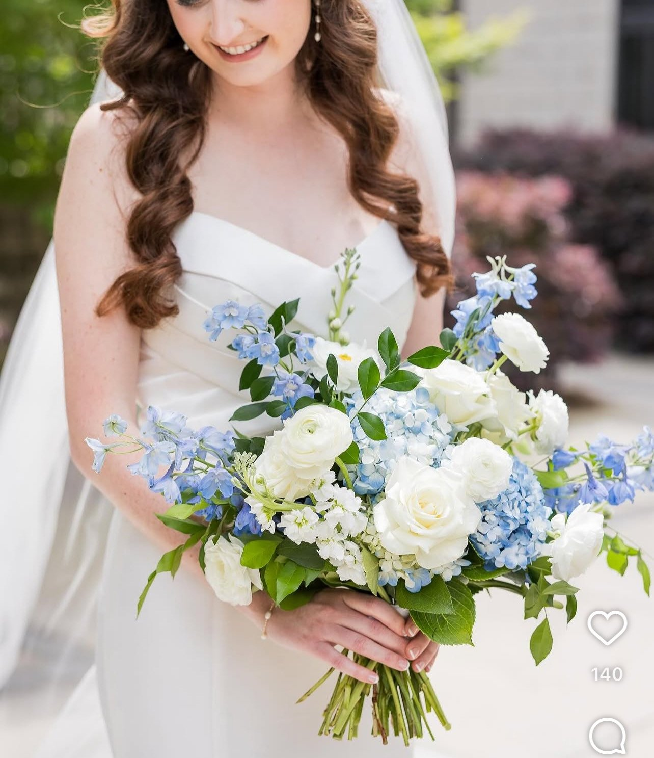 Bridal bouquet of white roses and ranunculus with blue delphinium and hydrangea, accented with lush greenery