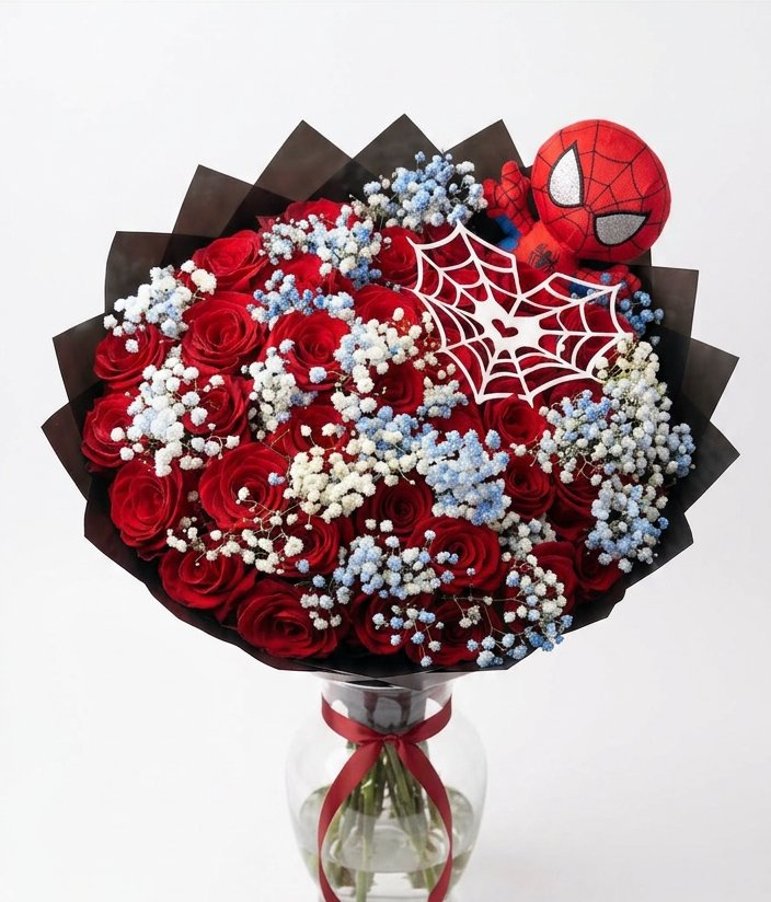 Red roses with red, white, and blue baby's breath in black wrapping, topped with a superhero plush and web accent