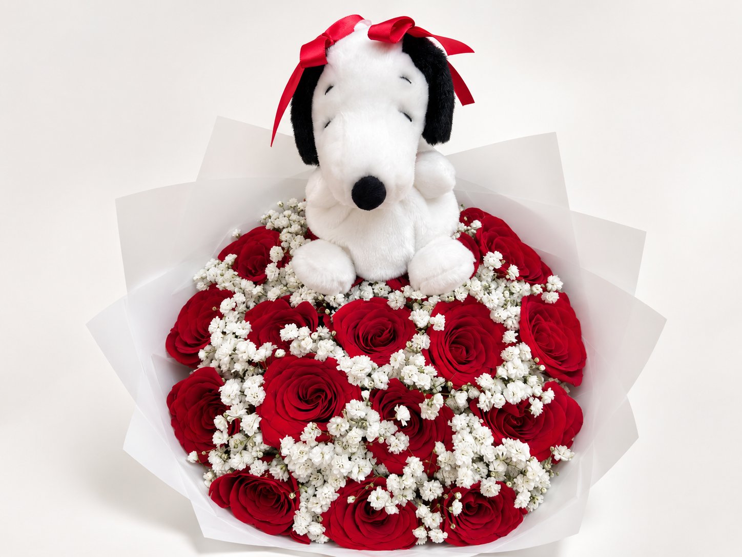 Cuddly black-and-white puppy plush sitting atop red roses and white baby's breath in white wrapping